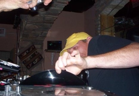 Extreme low-angle close-up of DJ Natural Nate® in yellow hat bent over the turntable scratching
